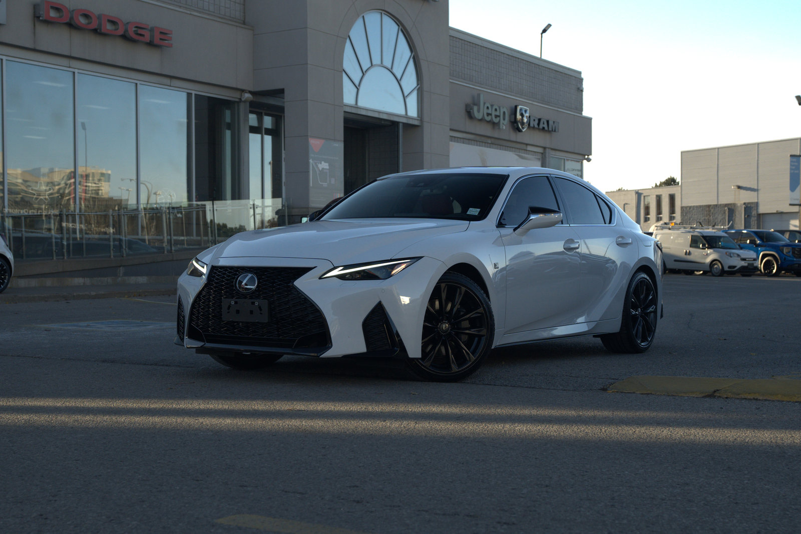 The same 2023 Lexus IS straight off the camera, parked in front of a dealership building.